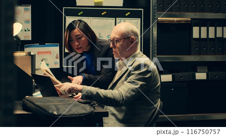 Inspectors team reviewing case information and reading witness statements to create a profile for the suspect. Detectives look into forensic evidence in police archive room, criminology. Camera A. Inspectors team reviewing case information and reading witness statements to create a profile for the suspect. Detectives look into forensic evidence in police archive room, criminology. Camera A. 116750757