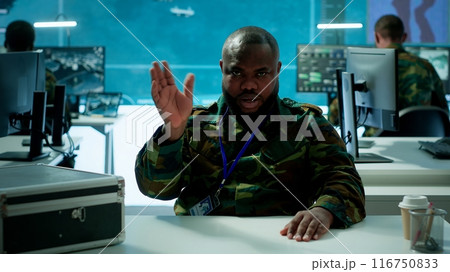 Military officer participates in a secure videoconference call in modern command center, transmitting live satellite information. Federal collaboration for national security operations. Camera A. Military officer participates in a secure videoconference call in modern command center, transmitting live satellite information. Federal collaboration for national security operations. Camera A. 116750833