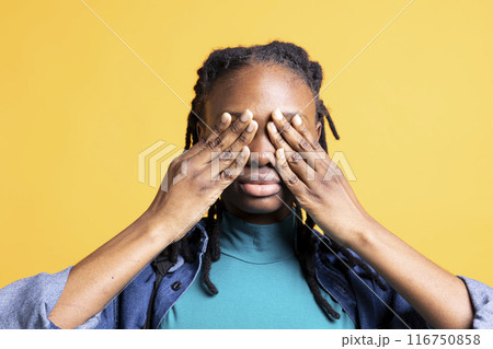 Tired BIPOC young girl covering face with palms, exhausted after long day at school. Close up shot of teenager in need of break, obstructing eyes with hand, isolated over studio background 116750858