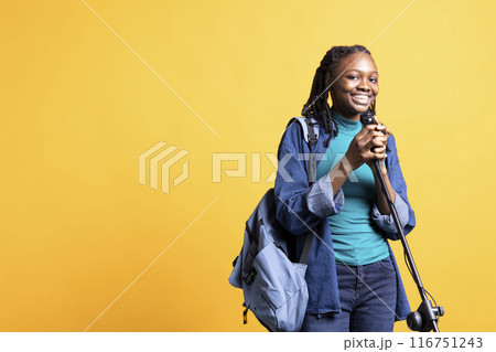 Portrait of smiling young presenter with backpack talking in microphone, addressing audience, studio background. Jolly school council president using mic, doing speech for students Portrait of smiling young presenter with backpack talking in microphone, addressing audience, studio background. Jolly school council president using mic, doing speech for students 116751243