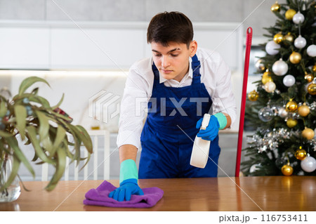 Man in uniform is ready to clean table in home before Christmas celebration Man in uniform is ready to clean table in home before Christmas celebration 116753411