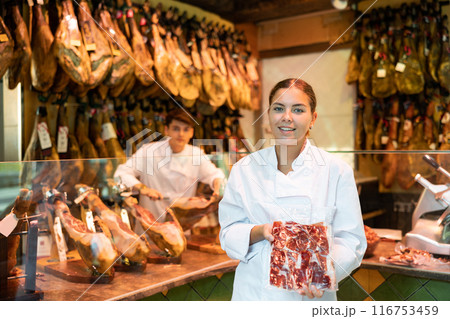 Young salesgirl of butcher shop offering package of sliced Iberian jamon 116753459