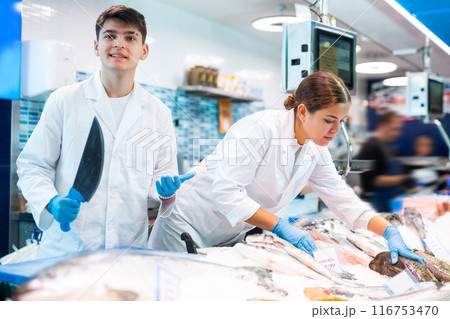 Seller with knife cut fish in supermarket near counter 116753470