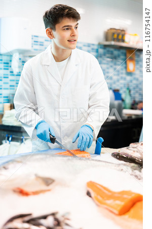 Proficient salesman cutting fish fillet in fish store 116754147