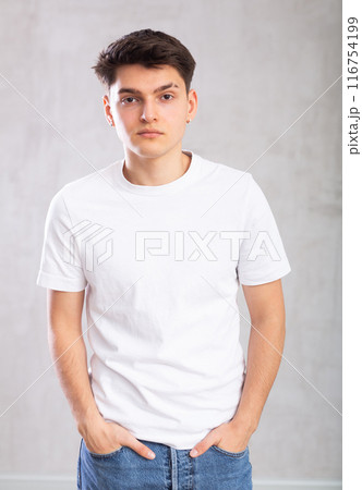 Confident young man posing against background of grey unicolored wall Confident young man posing against background of grey unicolored wall 116754199