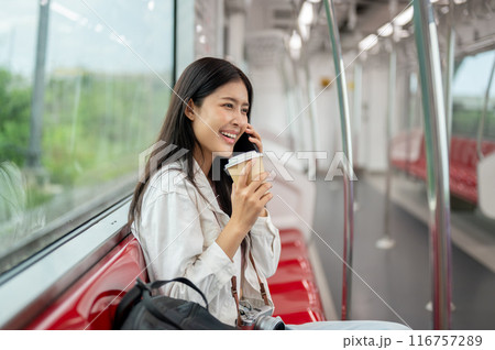 A beautiful, happy young Asian female passenger is talking on the phone while sitting in a sky train 116757289