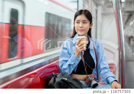 A happy Asian female passenger is sipping coffee while enjoying the view outside of a sky train. 116757303