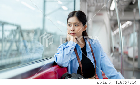 A positive, thoughtful Asian female is gazing at the view outside while commuting by sky train. A positive, thoughtful Asian female is gazing at the view outside while commuting by sky train. 116757314