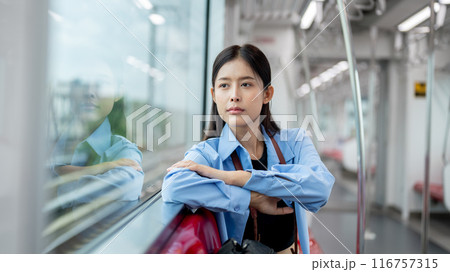 A positive, thoughtful Asian female is gazing at the view outside while commuting by sky train. 116757315