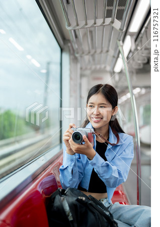A happy Asian female traveller is enjoying taking pictures with her camera on a sky train. 116757321