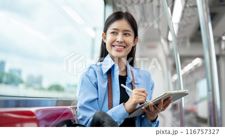 A female passenger is looking at the view outside while using her digital tablet on a sky train. 116757327
