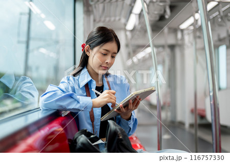 A beautiful Asian woman is using her digital tablet while taking the sky train somewhere. 116757330