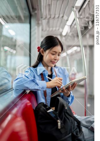 A beautiful Asian woman is using her digital tablet while taking the sky train somewhere. 116757331