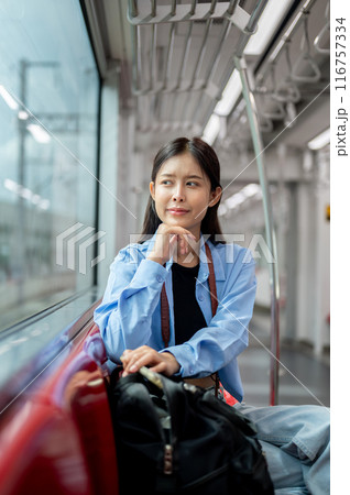 An Asian woman is taking the sky train somewhere, sitting on a seat and looking at the view outside. 116757334