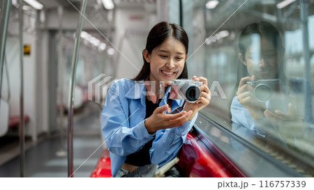 A happy Asian female tourist is taking a picture with her camera while taking the sky train. 116757339
