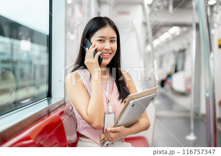 A beautiful Asian businesswoman is talking on the phone while taking a sky train to work. 116757347