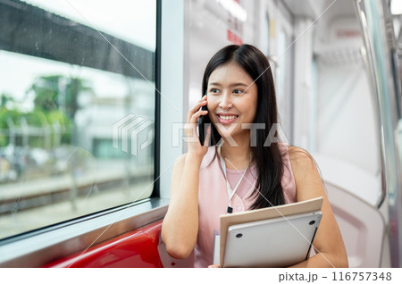 A beautiful Asian businesswoman is talking on the phone while taking a sky train to work. 116757348