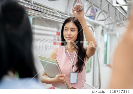 A positive Asian businesswoman is taking a sky train to work, holding a handrail. A positive Asian businesswoman is taking a sky train to work, holding a handrail. 116757352