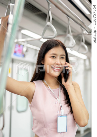A businesswoman is talking on the phone and holding a handrail while taking a sky train to work. A businesswoman is talking on the phone and holding a handrail while taking a sky train to work. 116757354