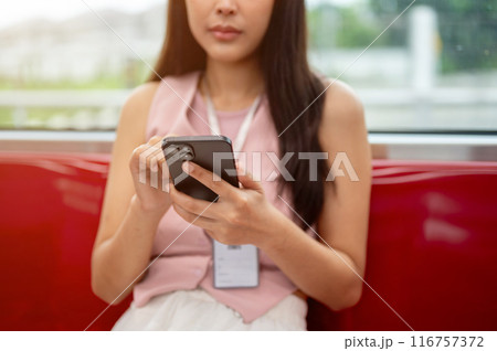 Cropped image of a thoughtful Asian female reading messages on her phone while taking the sky train. 116757372