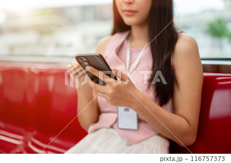 Cropped image of a thoughtful Asian female reading messages on her phone while taking the sky train. 116757373