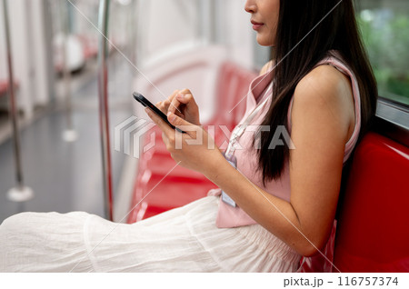 Thoughtful Asian female sitting at a seat, reading messages on her phone while taking the sky train. Thoughtful Asian female sitting at a seat, reading messages on her phone while taking the sky train. 116757374