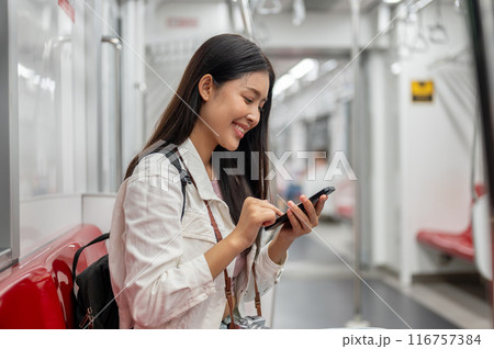 A happy Asian female tourist is chatting on the phone while sitting on a sky train or underground. 116757384