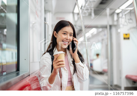 A happy Asian female tourist is talking on the phone while taking a sky train or metro train. 116757396