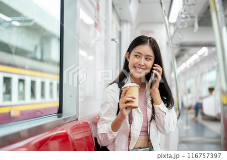 A happy Asian female tourist is talking on the phone while taking a sky train or metro train. 116757397