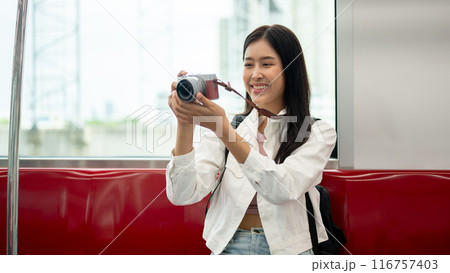 An Asian female tourist is taking pictures with her camera while commuting in a city on a sky train. 116757403