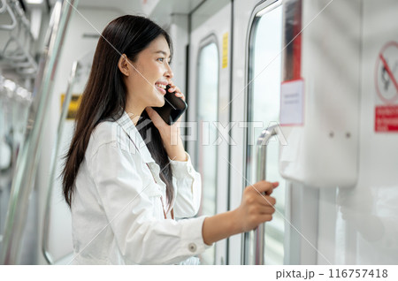 An attractive Asian woman is talking on the phone while holding onto a stanchion in a sky train. 116757418