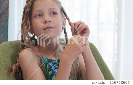 Teenage girl unbraiding pigtails in room on chair. Beauty and hair care.  116758667