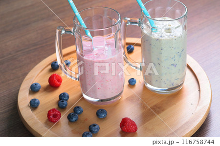 Milkshake in glass with tube on wooden stand. Raspberries and blueberries. Healthy food and nutrition.  116758744