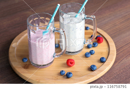 Milkshake in glass with tube on wooden stand. Raspberries and blueberries. Healthy food and nutrition.  116758791