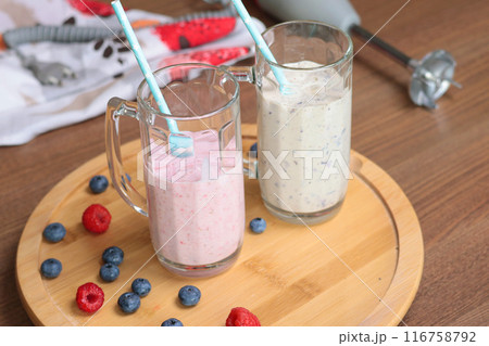 Milkshake in glass with tube on wooden stand. Raspberries and blueberries. Healthy food and nutrition. Milkshake in glass with tube on wooden stand. Raspberries and blueberries. Healthy food and nutrition. 116758792
