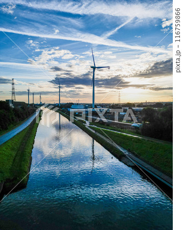 Wind turbines are installed along a canal, creating reflections under a scenic sunset sky 116759866