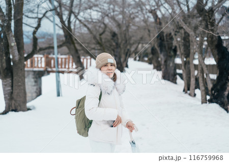 Woman tourist sightseeing sakura trees with snow. Happy traveler travel near Hinokinai River riverbank in winter season locate in Kakunodate town, Semboku District, Akita Prefecture, Japan Woman tourist sightseeing sakura trees with snow. Happy traveler travel near Hinokinai River riverbank in winter season locate in Kakunodate town, Semboku District, Akita Prefecture, Japan 116759968