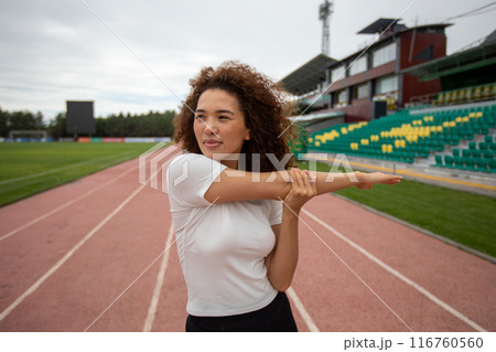 Beautiful curly girl warms up on the sports ground 116760560