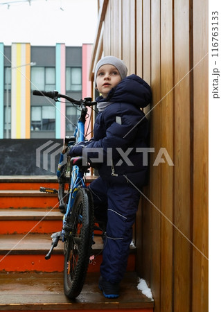 A Caucasian boy asked to take his bike for a walk in winter A Caucasian boy asked to take his bike for a walk in winter 116763133