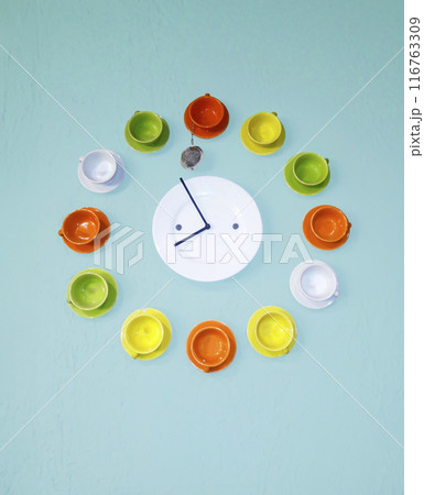 Wall clock consisting of cups and saucers on a blue wall. Time concept and tea time Wall clock consisting of cups and saucers on a blue wall. Time concept and tea time 116763309