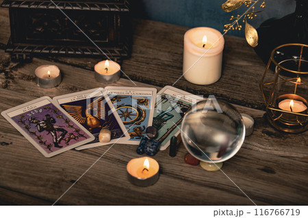 Close-up of a tarot card arrangement with a crystal ball and flickering candles on an aged wooden surface. 116766719