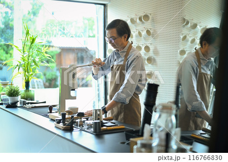 Senior male barista wearing apron making hot espresso shot from flair espresso coffee maker 116766830