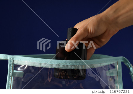 Black bottle of men's perfume in hand and cosmetic bag on dark blue background, close up Black bottle of men's perfume in hand and cosmetic bag on dark blue background, close up 116767221