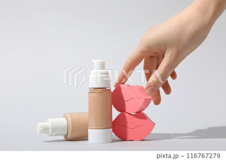 Bottles with foundation, female hand and cosmetic sponges on white background 116767279