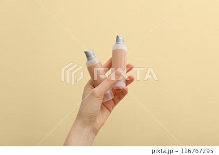 Bottles with foundation in female hands on beige background 116767295