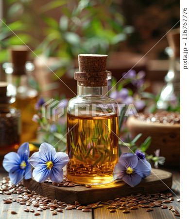 Bottle flaxseed oil in foreground, flax seeds and flowers scattered around, blurred countryside 116767776