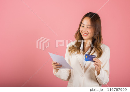 Portrait of happy Asian young woman holding paper calculating bills on hand and credit card for payment, female person she hold bill or paperwork, studio shot isolated on pink background Portrait of happy Asian young woman holding paper calculating bills on hand and credit card for payment, female person she hold bill or paperwork, studio shot isolated on pink background 116767999