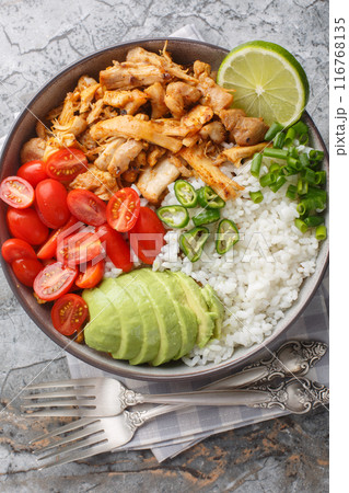 Bowl with pulled spicy chicken, rice, cherry tomatoes, avocado, jalapano pepper close-up on the table. Vertical top view 116768135