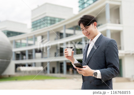 Young Professional Man in Suit Holding Coffee and Smartphone Outside Modern Office Building Young Professional Man in Suit Holding Coffee and Smartphone Outside Modern Office Building 116768855