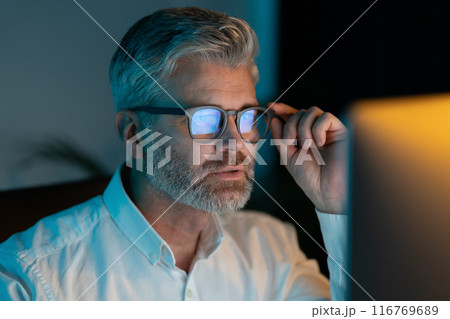 Mature Man Focusing on Computer Screen While Working Late at Night 116769689